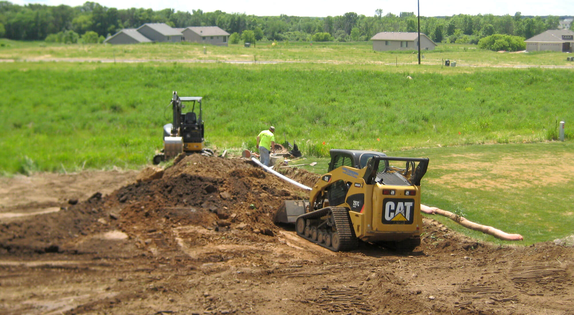 Excavating crew using a mini excavator and a bobcat to place underground pipe